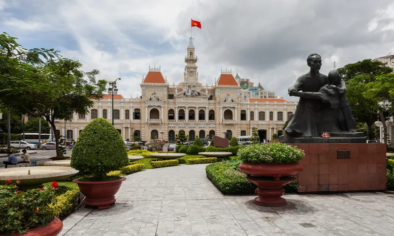 The colonial-style Ho Chi Minh City Hall with its clock tower stands beyond a statue and manicured garden.