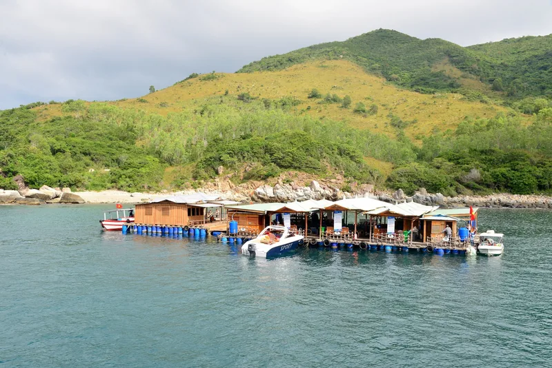 A floating wooden restaurant on barrels sits in a bay near green hills off the coast of Nha Trang, Vietnam.
