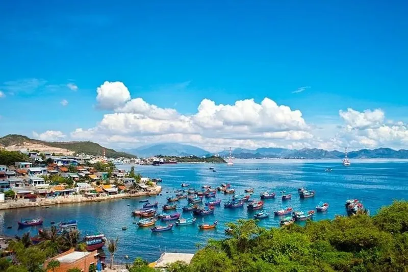 A coastal fishing village in Nha Trang with colorful boats moored in a bay under a bright blue sky.