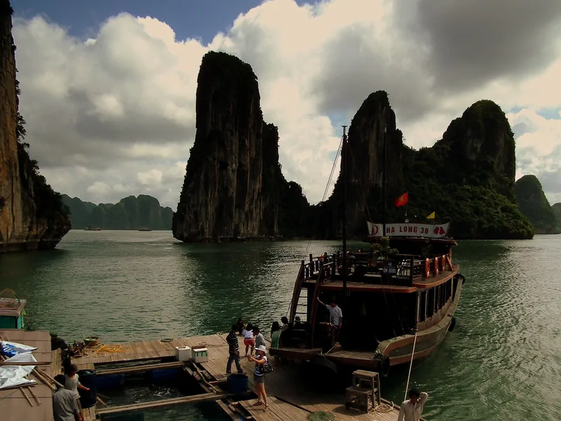 A wooden tourist junk boat docks at a floating platform among towering limestone karsts in Ha Long Bay.