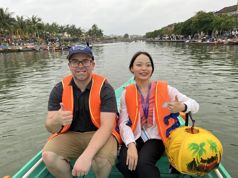 Two travelers in orange life vests give thumbs up on a boat along the Thu Bon River in Hoi An.