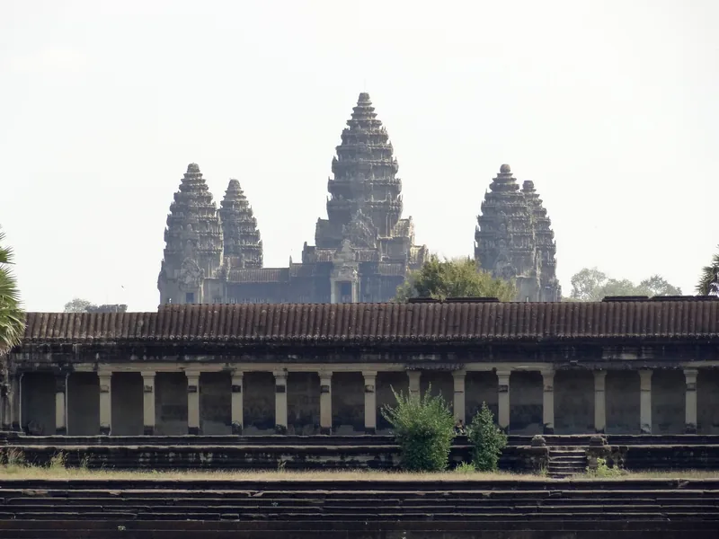 The five stone towers of Angkor Wat rise above a colonnaded gallery under a hazy sky in Siem Reap.