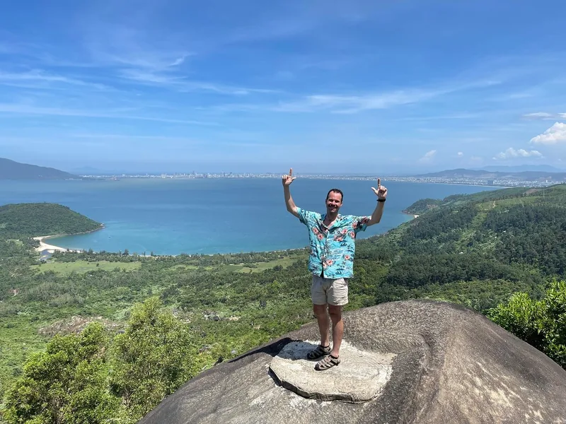 A traveler poses on a rocky summit overlooking Da Nang bay along the Hai Van Pass route.
