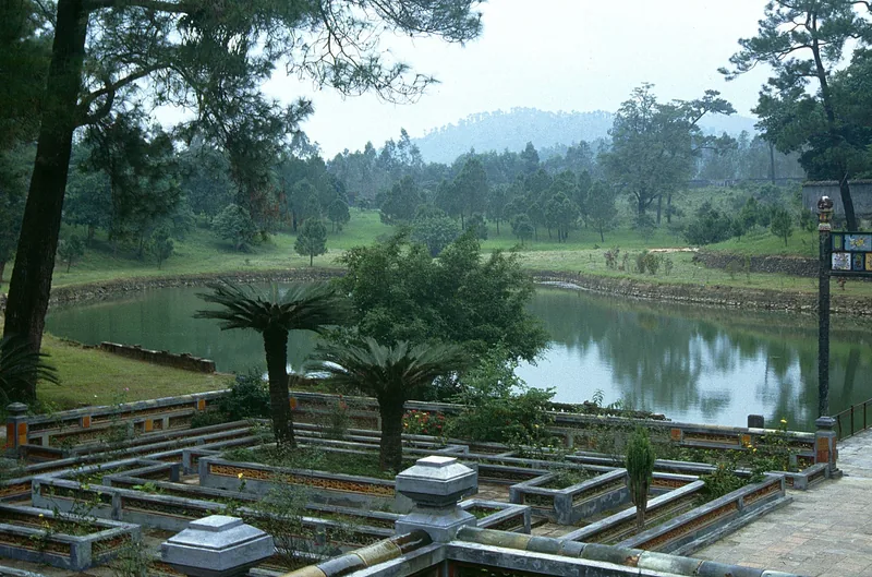 A tranquil pond and terraced garden surrounded by pine trees at a royal tomb site in Hue.