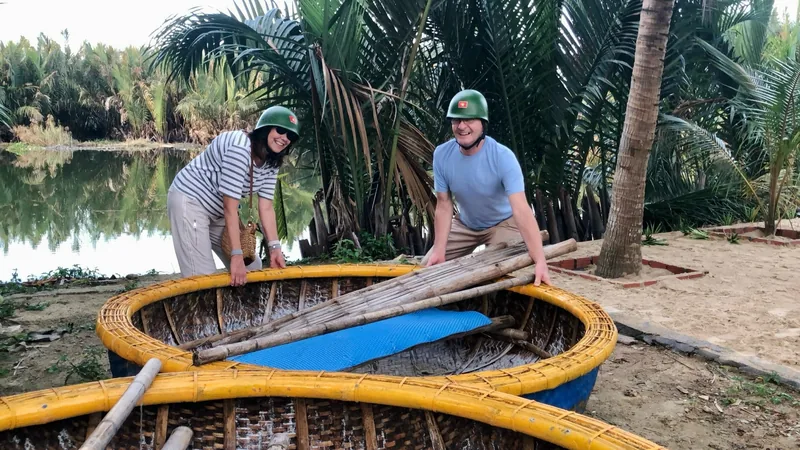 Tourists in helmets prepare a traditional round bamboo basket boat by a coconut palm lagoon near Hoi An.