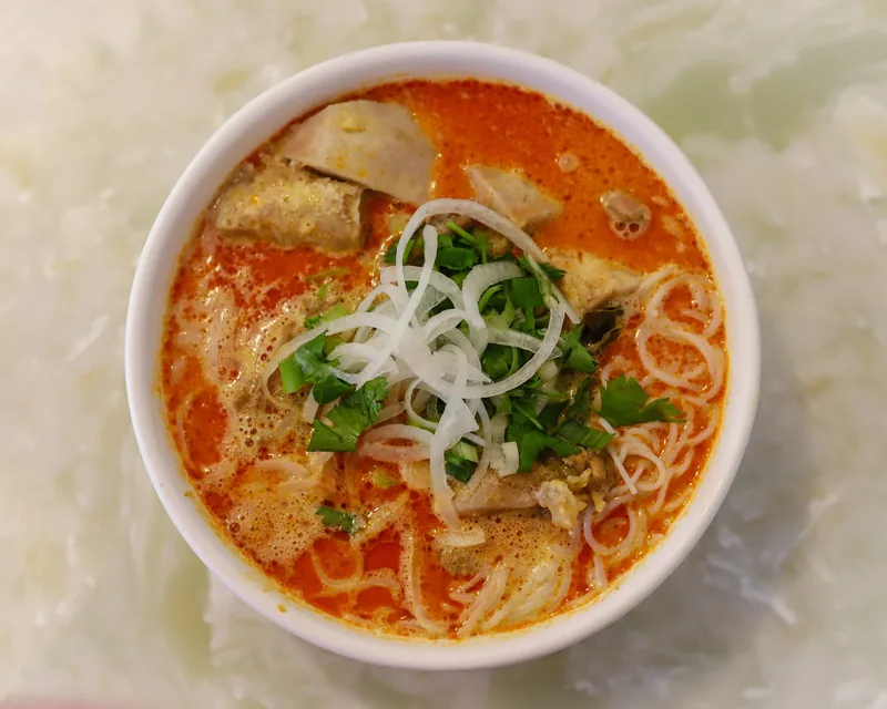 A bowl of Vietnamese chicken curry noodle soup topped with sliced onions and cilantro.