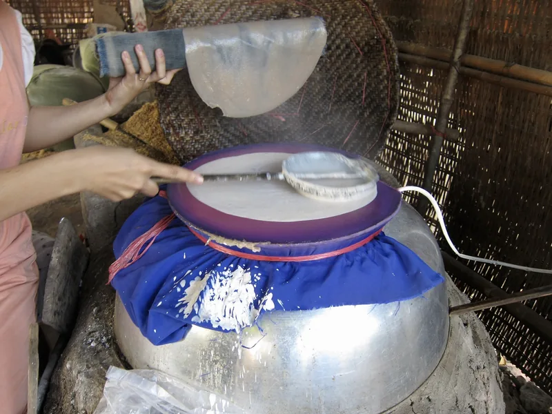 A woman spreads rice batter over a cloth-covered steamer to make traditional Vietnamese rice paper.