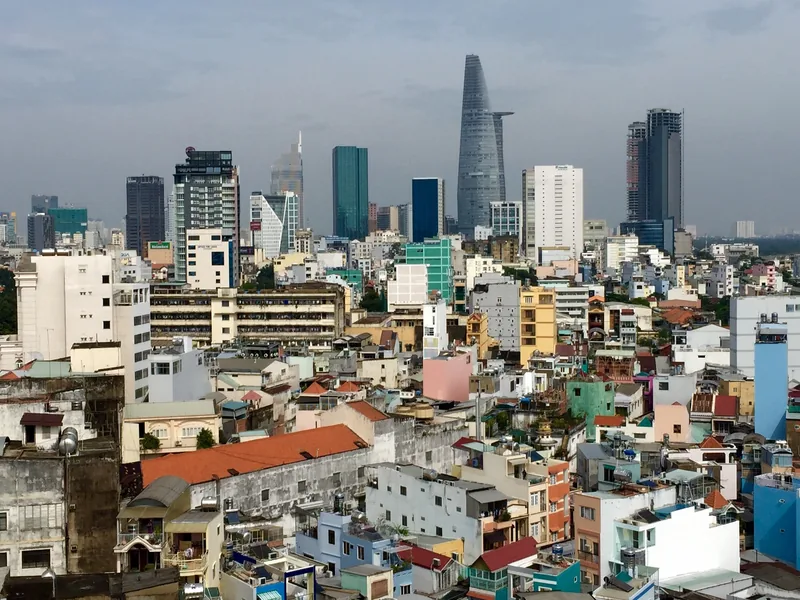 Aerial view of Ho Chi Minh City's dense skyline with colorful low-rise rooftops and the Bitexco Financial Tower rising.