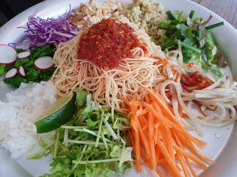 A plate of Vietnamese vermicelli topped with chili, peanuts, and fresh vegetables like carrot, cabbage, and lime.