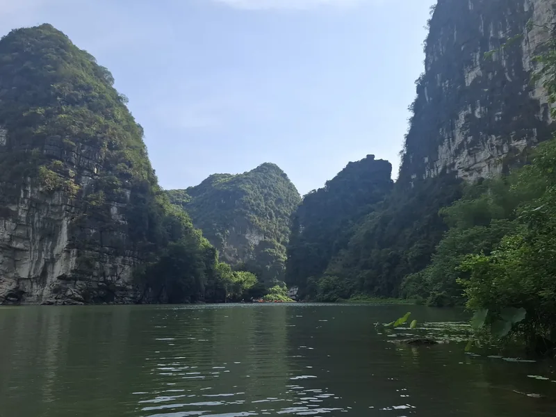 Limestone karst mountains rise above calm river water in Ninh Binh's Trang An landscape.