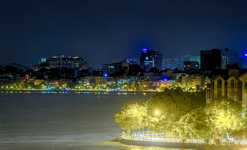 City skyline glows at night along the shore of West Lake in Hanoi.