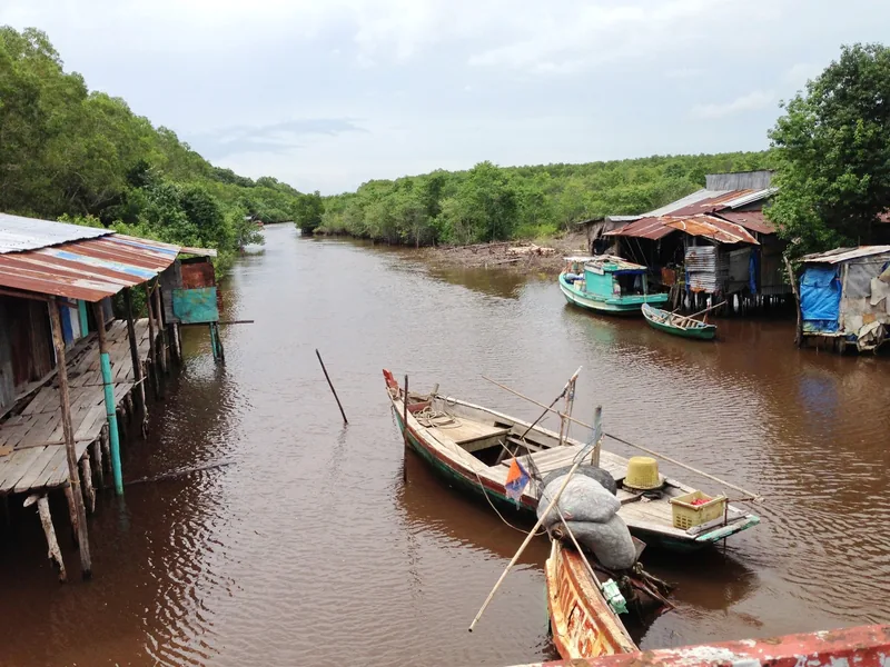 Wooden boats float on a muddy river lined with stilt houses in a fishing village on Phu Quoc.