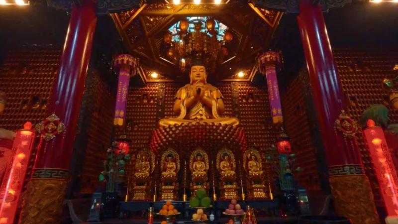 A golden Buddha statue sits above an ornate altar decorated with red pillars and lanterns inside a Saigon temple.