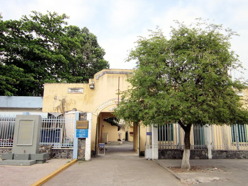 Yellow archway entrance gate of the old Can Tho prison, shaded by trees along the street.