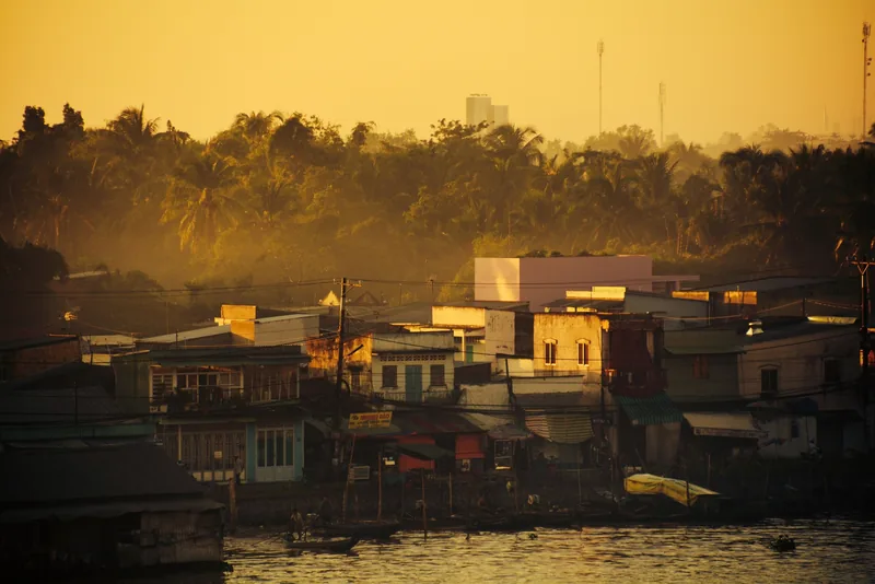 Golden sunset light bathes riverside houses and palm trees along the Can Tho River in Can Tho city.