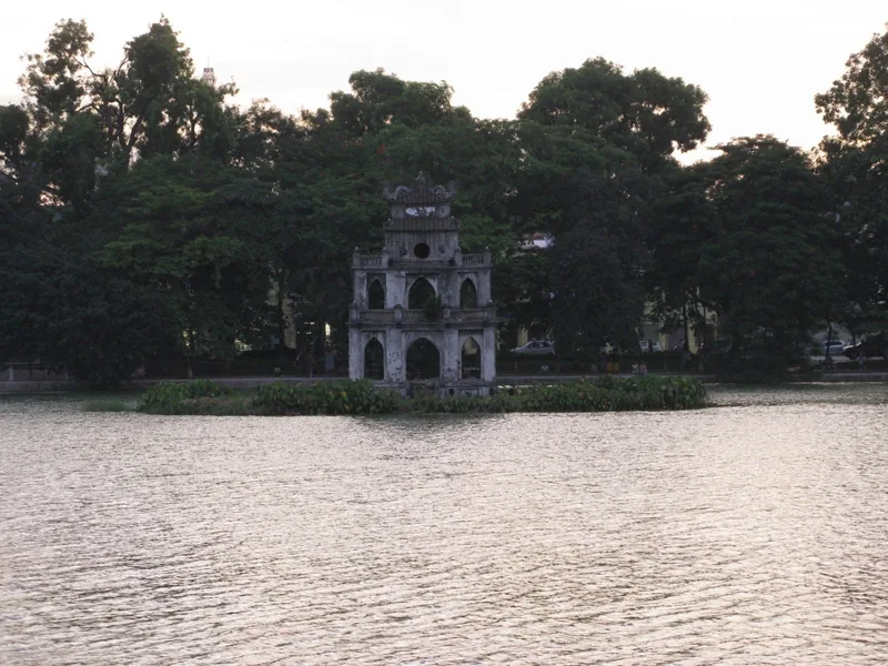 Turtle Tower stands on its small islet in Hoan Kiem Lake at dusk, surrounded by trees.