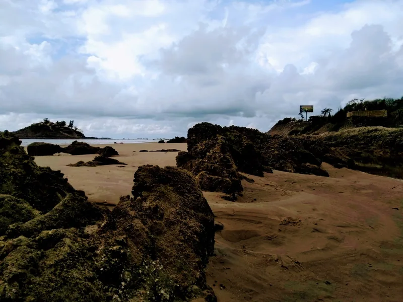 Dark volcanic rocks scatter across a sandy beach under a cloudy sky in Vung Tau.