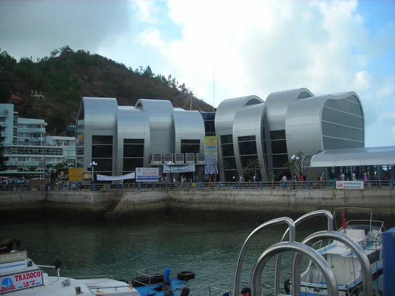 A modern silver, curved-roof ferry terminal building sits along the waterfront in Vung Tau, with boats moored in the.