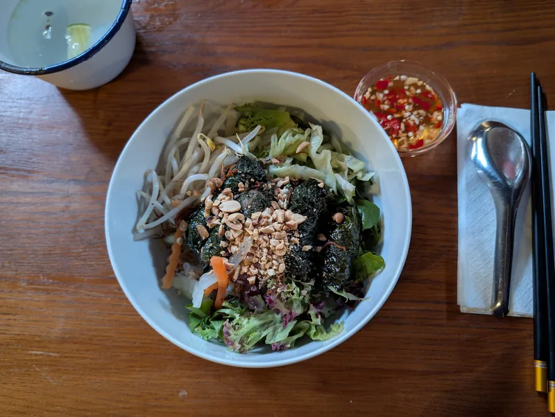 A bowl of Vietnamese noodle salad topped with grilled betel-leaf beef rolls, herbs, and crushed peanuts.